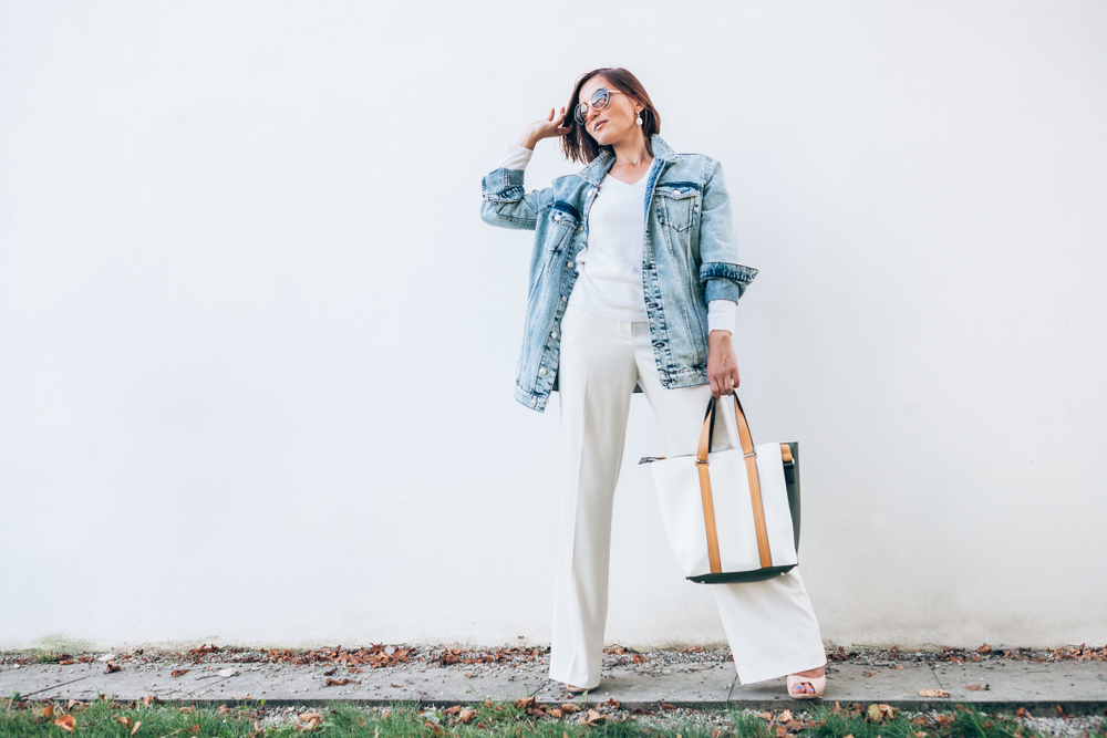 Stylish middle-age woman in white wide leg pants, sunglasses, and jean jacket