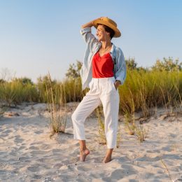 Stylish woman on the beach in white cropped linen pants and hat
