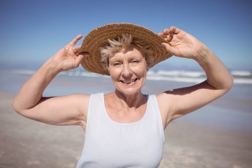 Happy senior woman on the beach in a tank top and hat