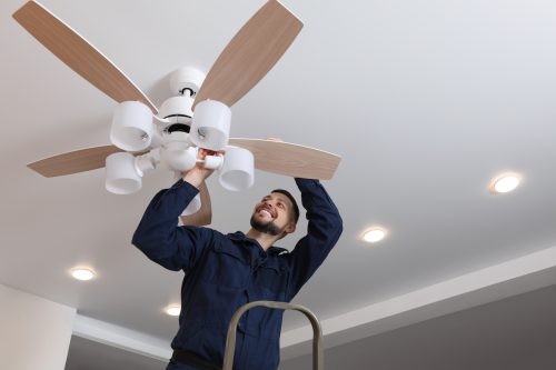 Electrician repairing ceiling fan with lamps indoors