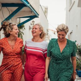 Three happy female friends walking through a European town on vacation, wearing colorful sundresses