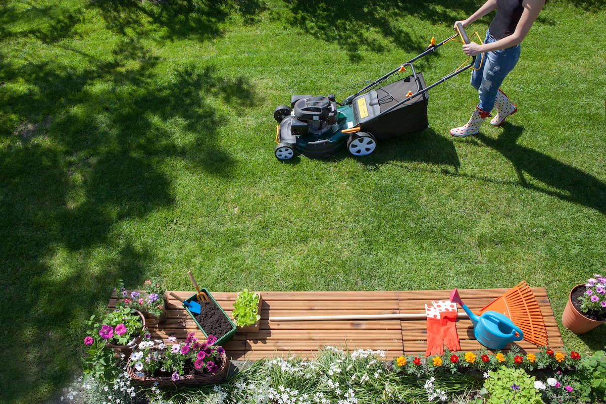 Woman wearing wellington boots mowing grass with lawn mower in the garden