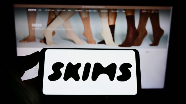A close up of a phone screen with the SKIMS logo above a computer screen with the SKIMS website
