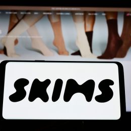 A close up of a phone screen with the SKIMS logo above a computer screen with the SKIMS website
