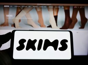 A close up of a phone screen with the SKIMS logo above a computer screen with the SKIMS website