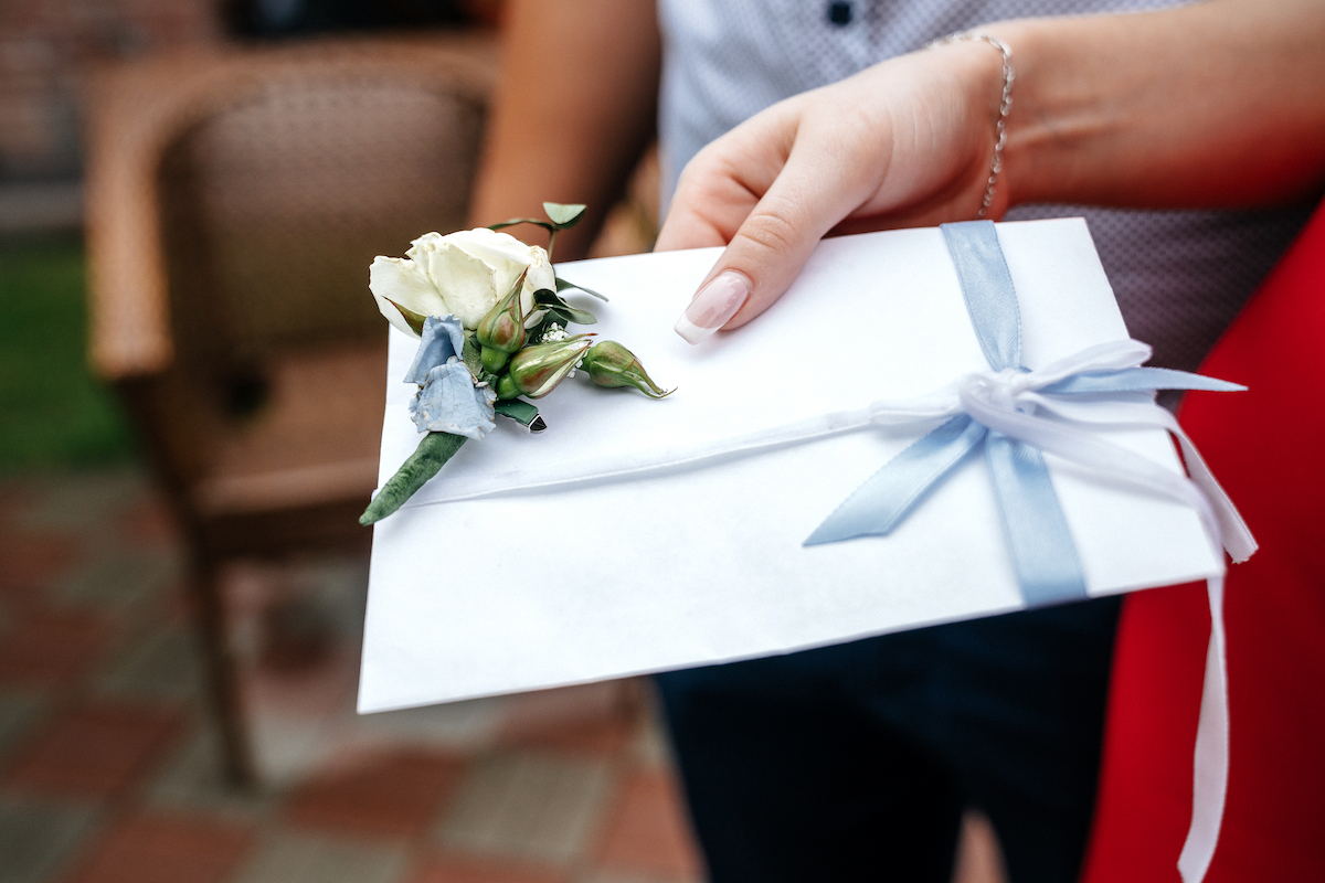 White wedding envelope with a boutonniere in the hand of a woman.