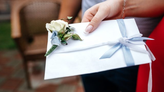 White wedding envelope with a boutonniere in the hand of a woman.