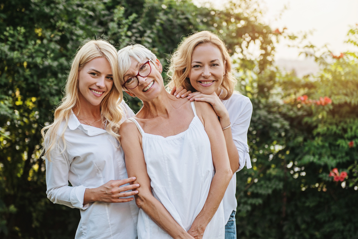 Woman and her two daughters hugging all wearing white outside.