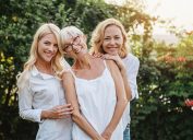 Woman and her two daughters hugging all wearing white outside.