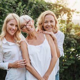 Woman and her two daughters hugging all wearing white outside.