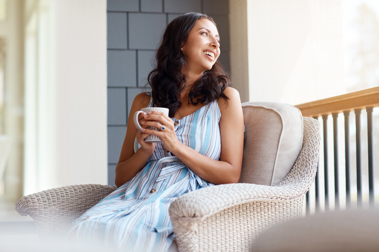 A woman drinking a cup of coffee or tea while sitting on her front porch