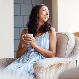 A woman drinking a cup of coffee or tea while sitting on her front porch