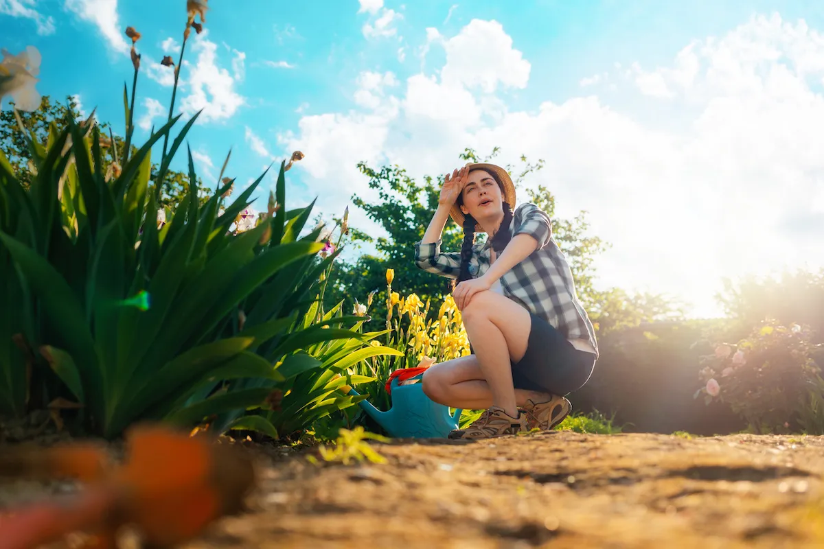 A young woman sits in the garden, wiping the sweat from her brow.