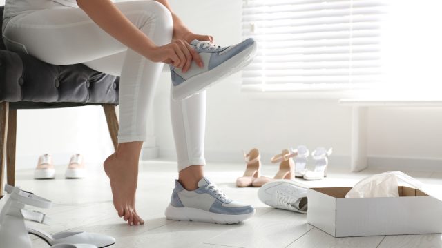Cropped view of a woman wearing white pants trying on shoes