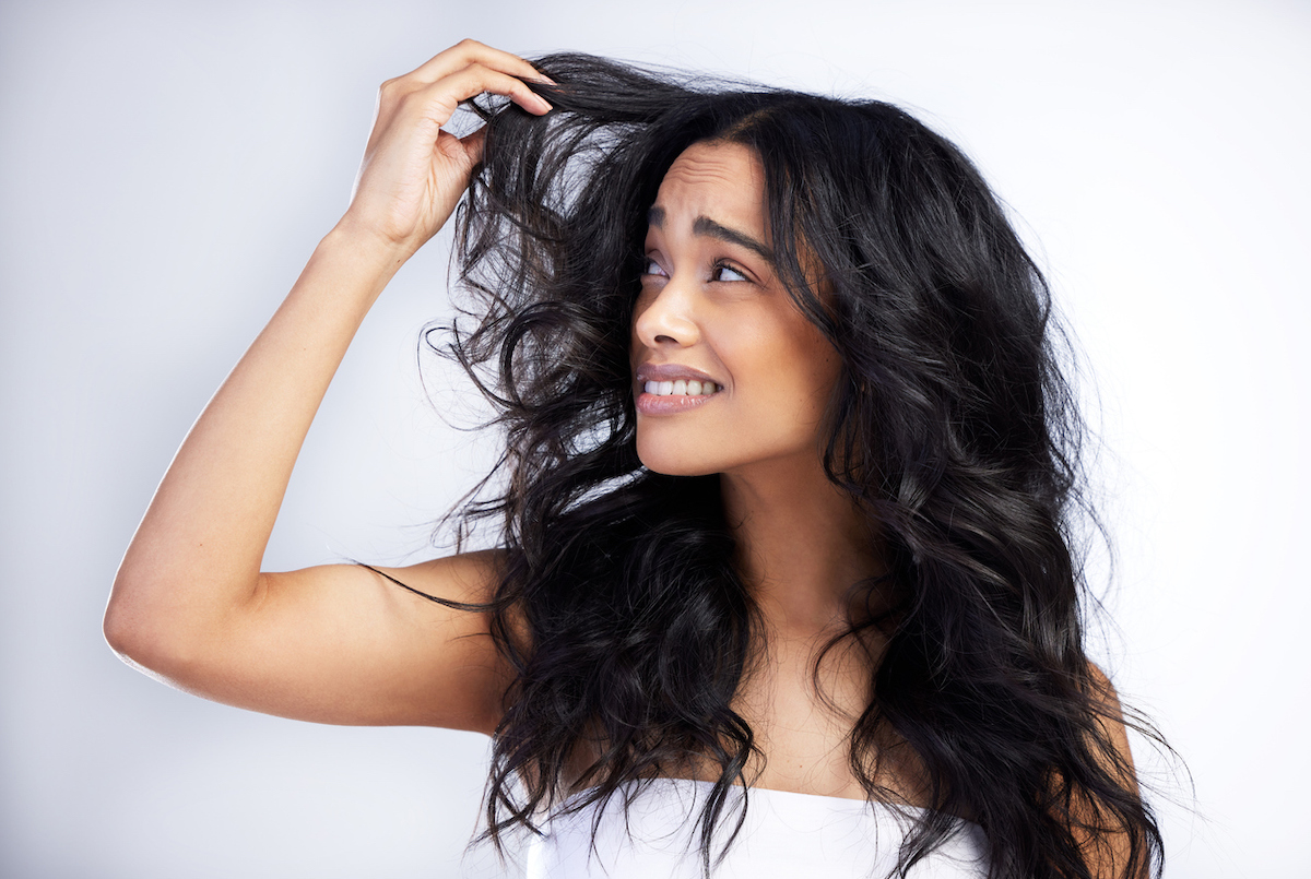 Woman wrapped in a white towel against a white background looking unhappily at her dark curly hair