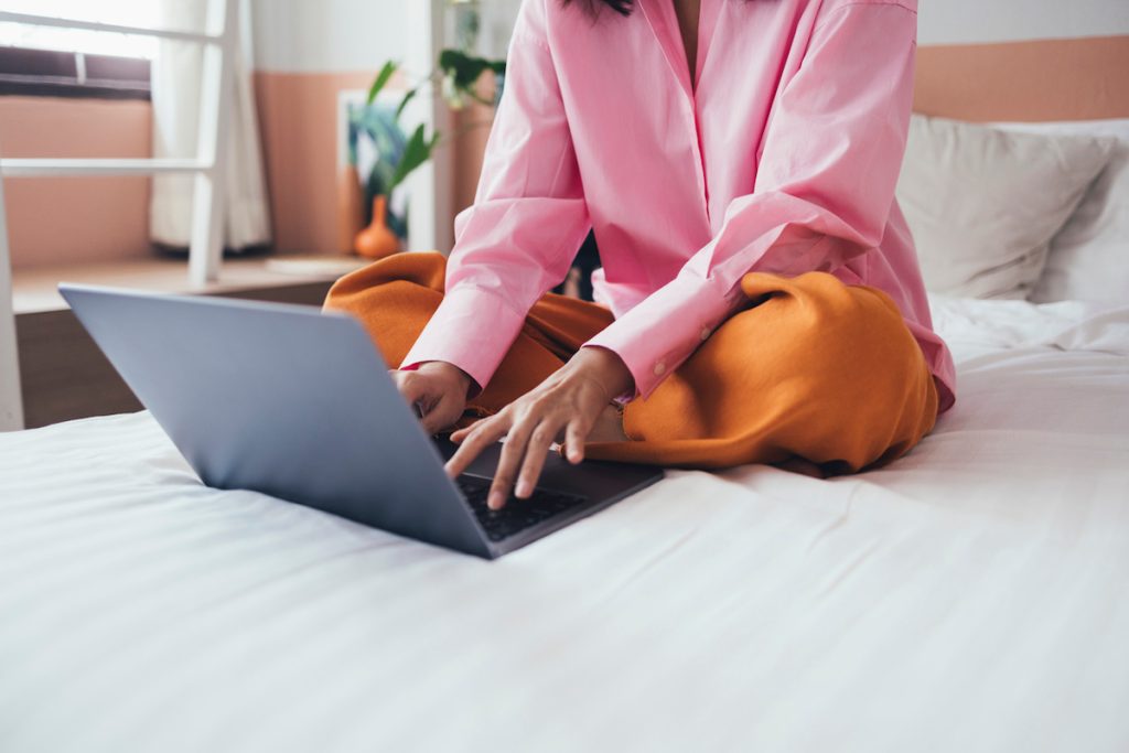 Woman sitting on made bed using laptop