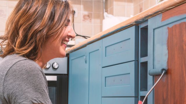 Smiling woman painting her kitchen cabinets blue