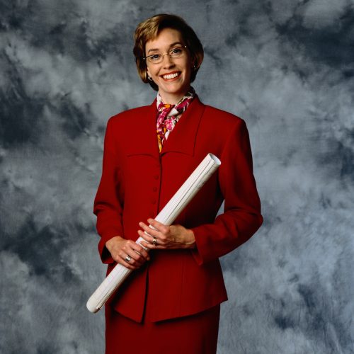 Woman posing in a red power suit against a gray background