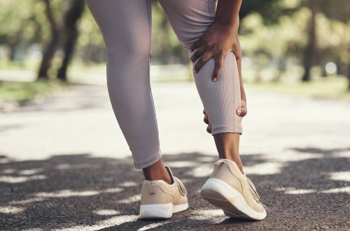 Close up of a woman in mauve leggings and sneakers, on a walk, clutching her calf.