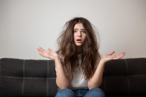 brunette young woman with tangled long hair looks desparate and unhappy with her hairstyle