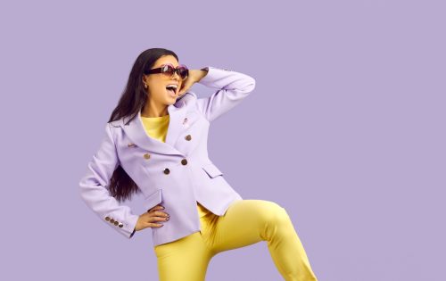Young woman wearing yellow paints with a light purple blazer, against a purple background