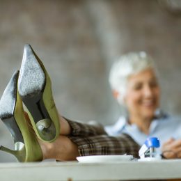 Close up of a woman with white hair's feet in high-heels resting on the table in the office.