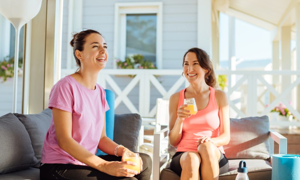 Two women sitting on their front porch drinking cocktails and smiling