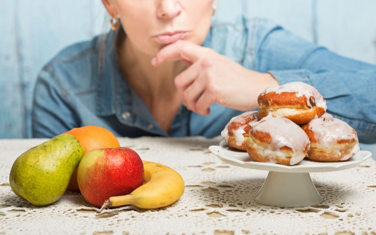 Woman choosing between fruit and sweets