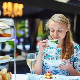 Beautiful young woman enjoying afternoon tea with selection of fancy cakes and sandwiches in a luxury Parisian restaurant
