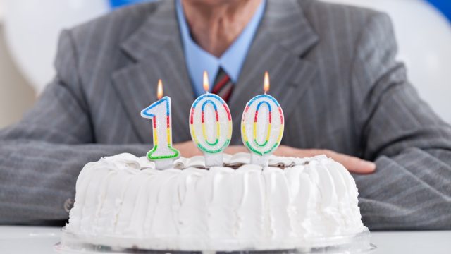 Man sitting behind cake with 100 birthday candle