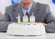 Man sitting behind cake with 100 birthday candle