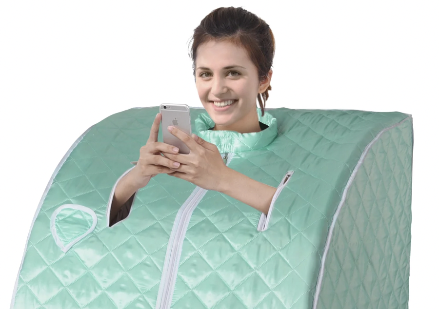 A woman using a portable sauna while smiling and looking at her phone