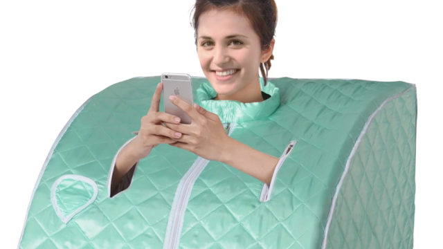 A woman using a portable sauna while smiling and looking at her phone