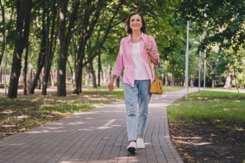 Mature woman wearing jeans and a pink shirt outside walking in a park.
