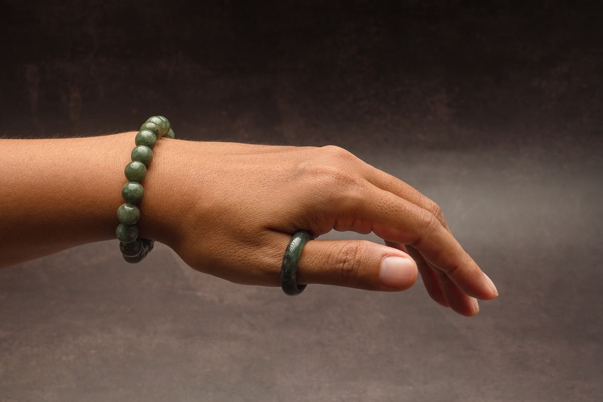 Jade bangle or bracelet on the wrist and a green jade ring on a finger against a black background. Close-up photo