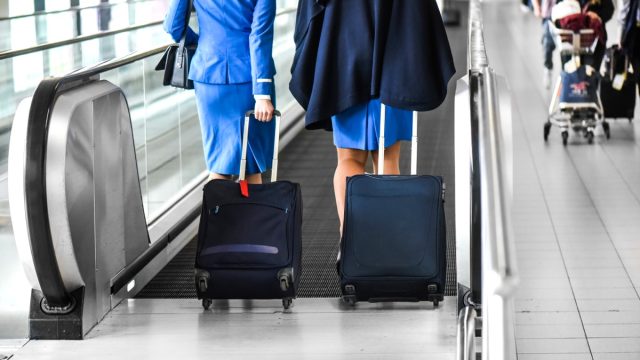 Two stewardess walk through escalator or quick movie stairs on airport lobby or station with suitcases.