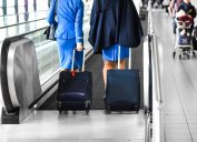 Two stewardess walk through escalator or quick movie stairs on airport lobby or station with suitcases.