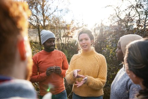 group of people talking in the woods with focus on woman asking question in yellow sweater