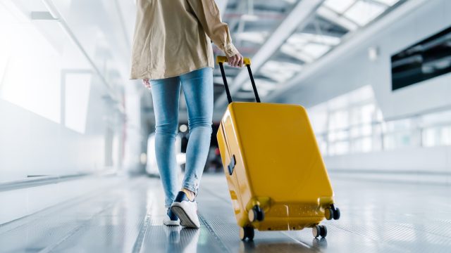 A close up of a person pulling a yellow wheeled suitcase through an airport