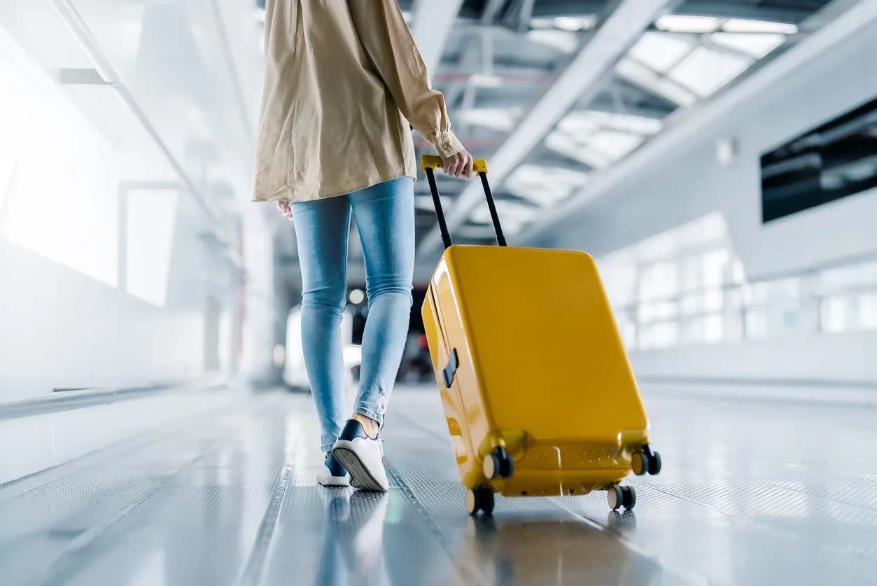 A close up of a person pulling a yellow wheeled suitcase through an airport