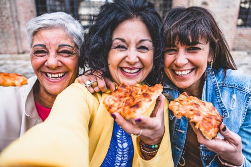 Three happy mature women eating pizza and taking selfie photo with smartphone