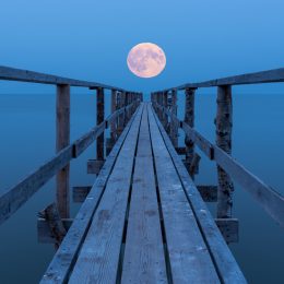 A full moon rising over a lake with a view down a long dock