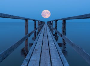 A full moon rising over a lake with a view down a long dock