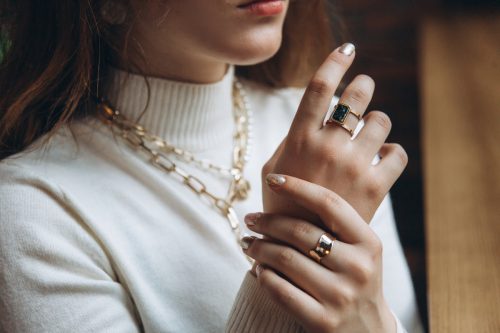 closeup of a woman in a cream turtleneck sweater wearing a gold necklace and two gold rings