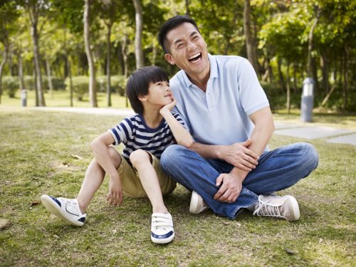 Young boy and father sitting in a park laughing