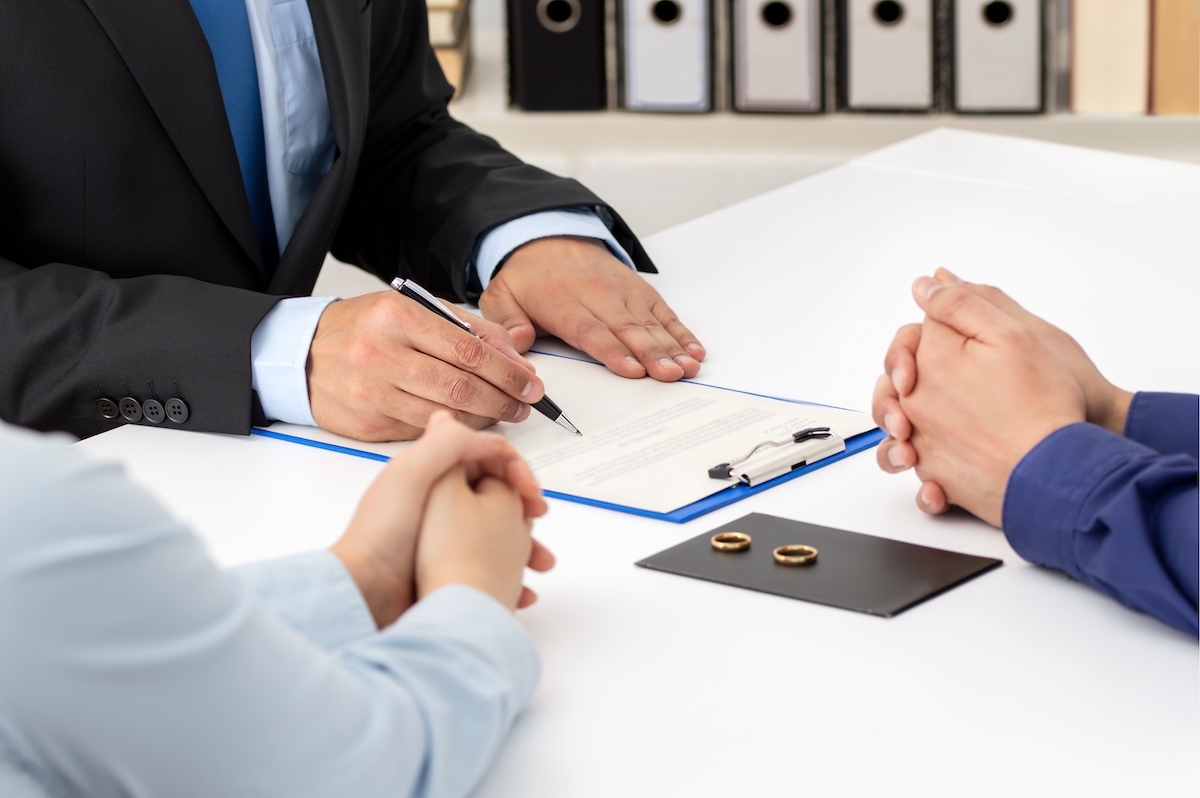 Close up of a couple signing divorce papers with attorney and their rings on the table