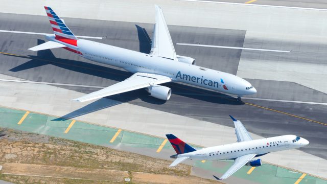 An American Airlines jet taxiing on the runway while a Delta Air Lines jet takes off