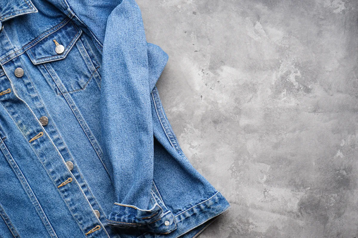 Classic jeans texture. Blue denim jacket on a gray background, space for text. Top view.