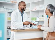 Healthcare, pharmacist and woman at counter with medicine or prescription drugs in hands at drug store. Health, wellness and medical insurance, man and customer at pharmacy for advice and pills.
