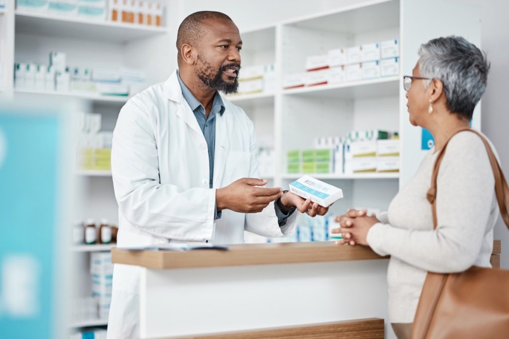 Male pharmacist holding medication and talking to female customer.